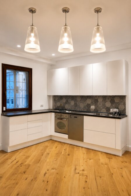 Cucina moderna su misura bianca con top scuro, pensili lineari, rivestimento decorativo, pavimento in legno e lampade a sospensione.