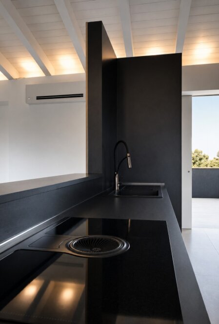 Dettaglio di cucina su misura con top nero, piano a induzione, cappa integrata e illuminazione sottotetto.