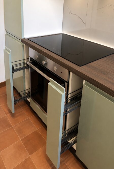 Dettaglio di cucina su misura con piano a induzione, top effetto legno, forno integrato e cassettoni estraibili aperti.